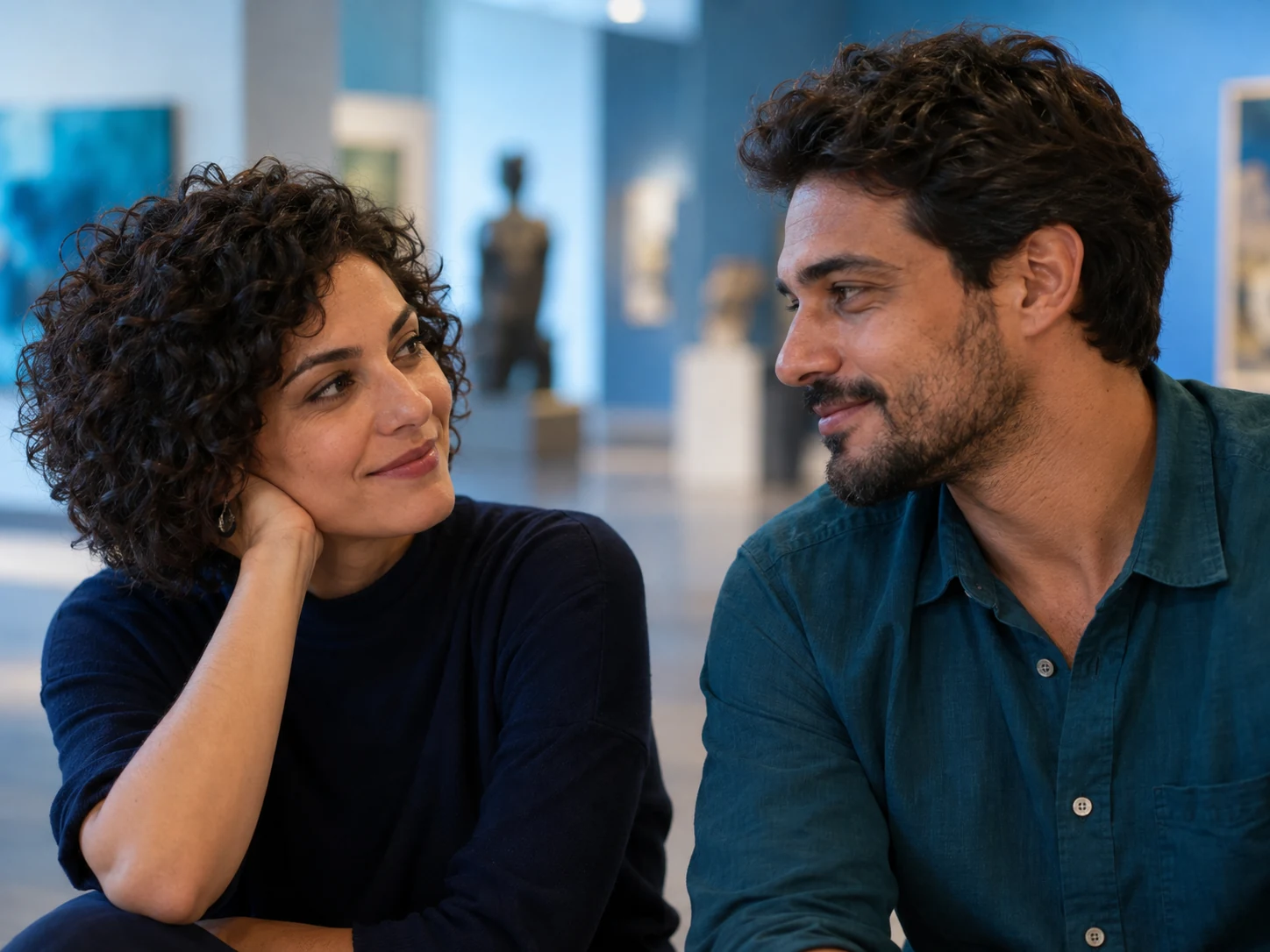 Duas pessoas adultas, vestidas, conversam e trocam olhares em um museu.